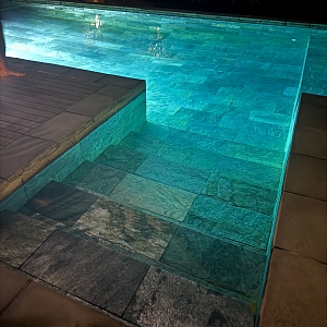 Современный бассейн, облицованный плиткой под сланец. Гладкая вода отражает свет, подчеркивая благородный серый оттенок отделки.